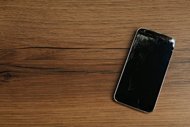 Photo of Damaged smartphone on wooden table, top view with space for text. Device repairing