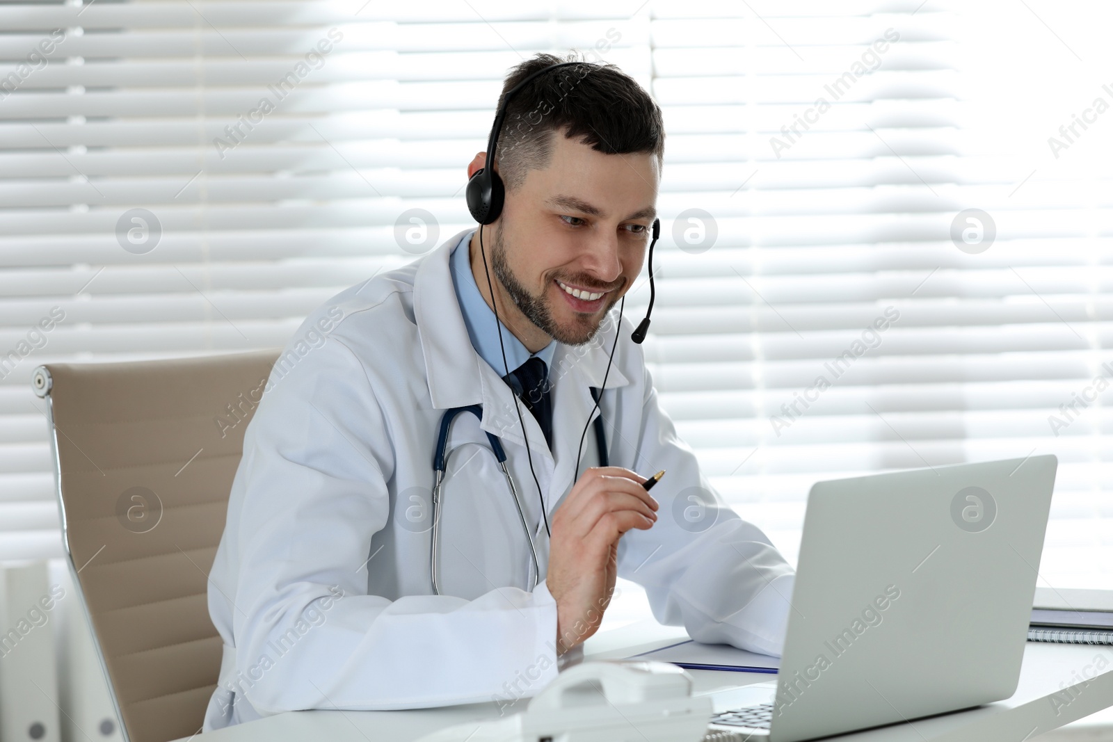 Photo of Doctor with headset consulting patient online at desk in clinic. Health service hotline