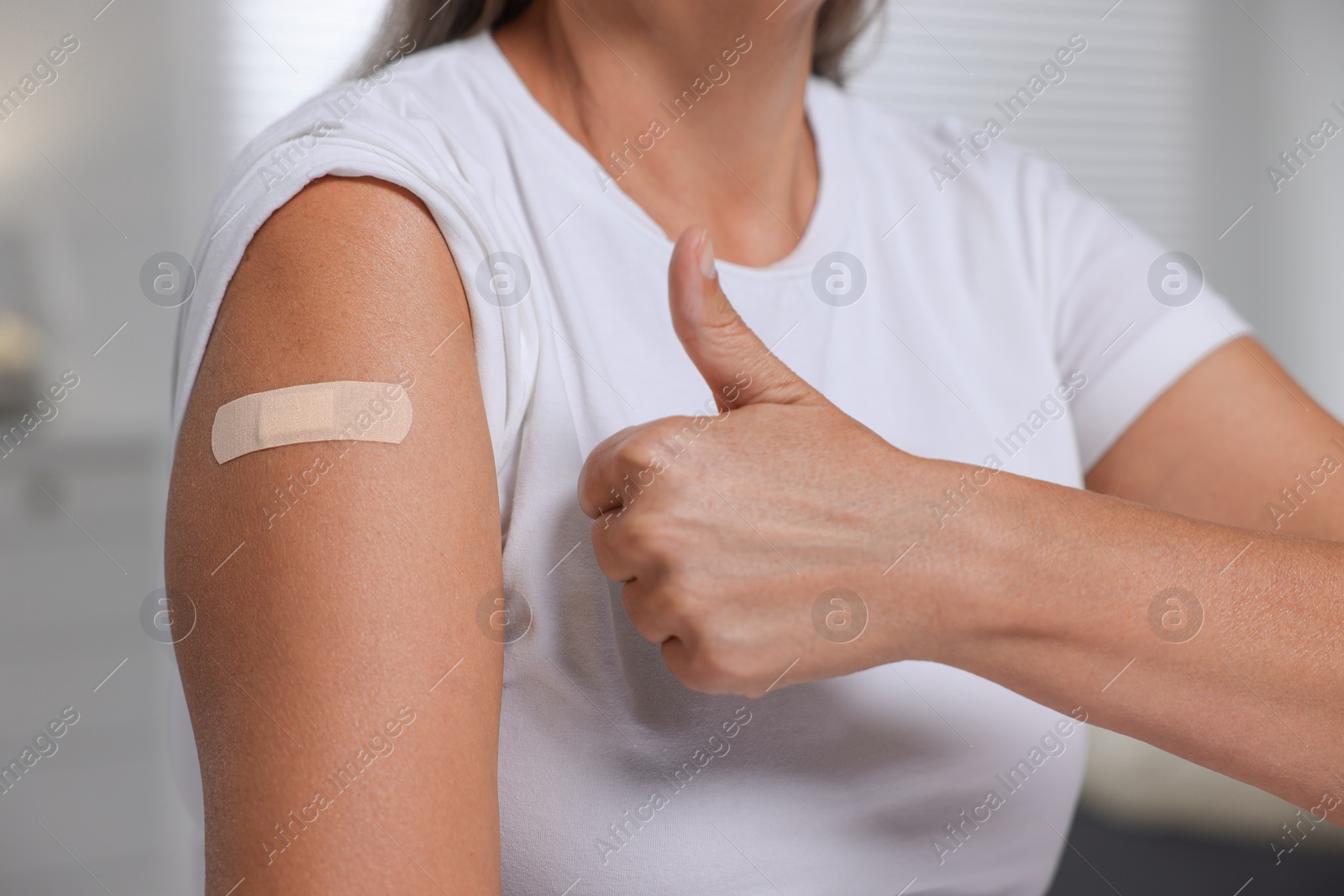 Photo of Woman with adhesive bandage on her arm after vaccination showing thumb up against blurred background, closeup