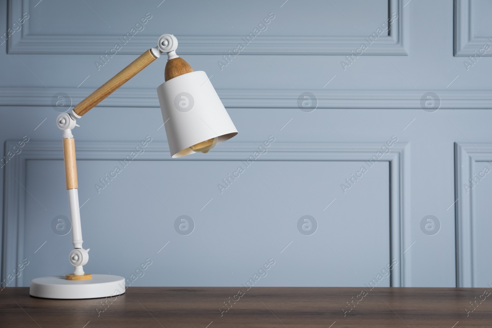 Photo of Stylish modern desk lamp on wooden table near light grey wall, space for text