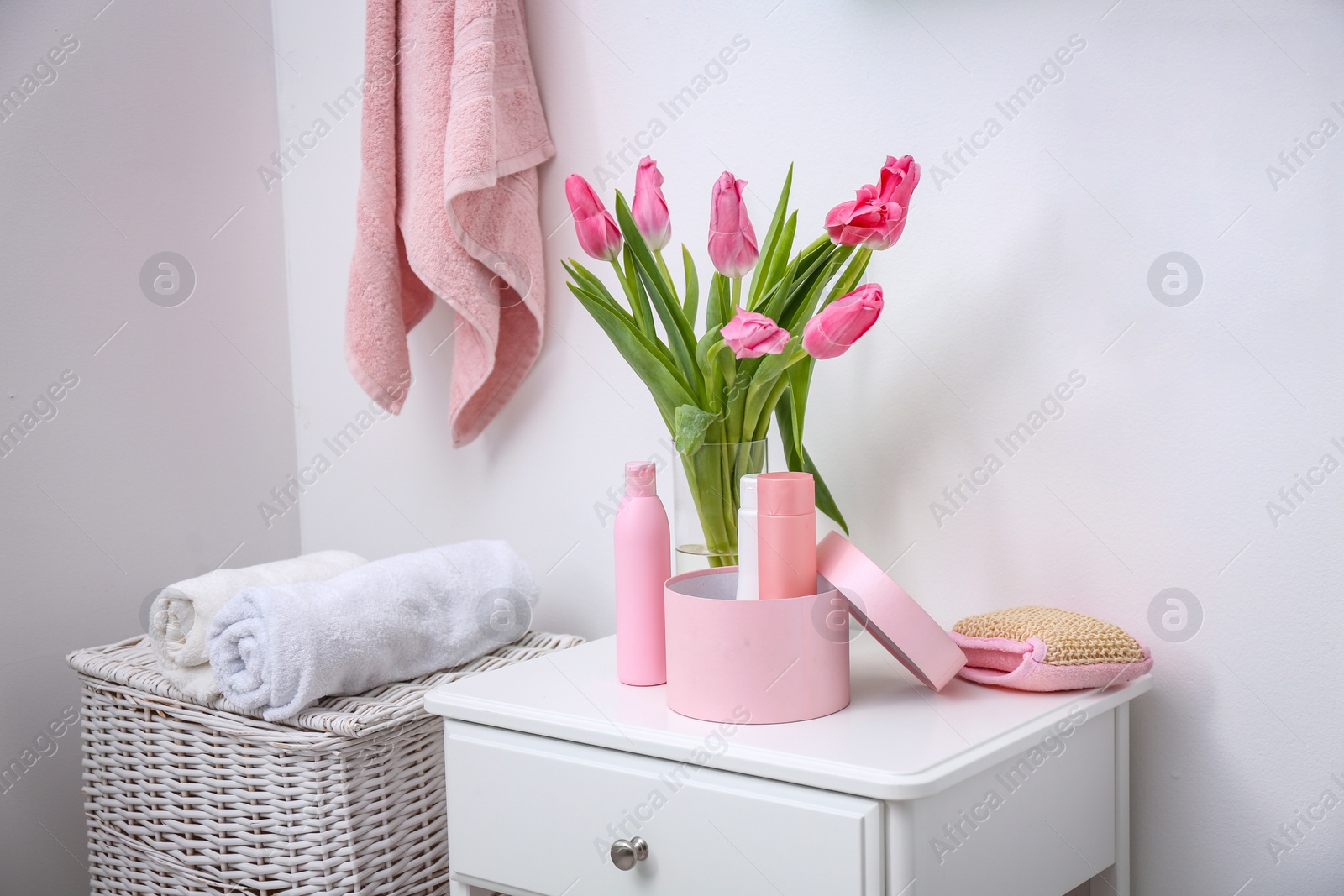 Photo of Fresh tulips and toiletries on cabinet in bathroom