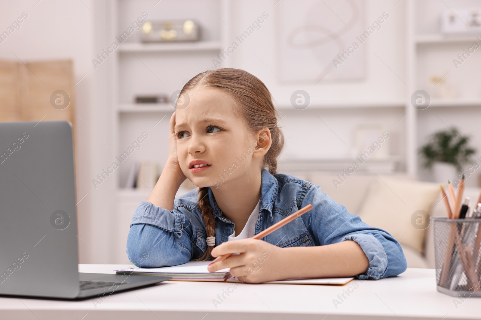 Photo of Little girl suffering from headache while doing homework at home