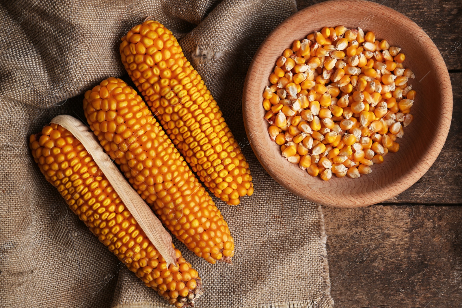 Photo of Delicious ripe corn cobs and bowl with seeds on wooden table, flat lay