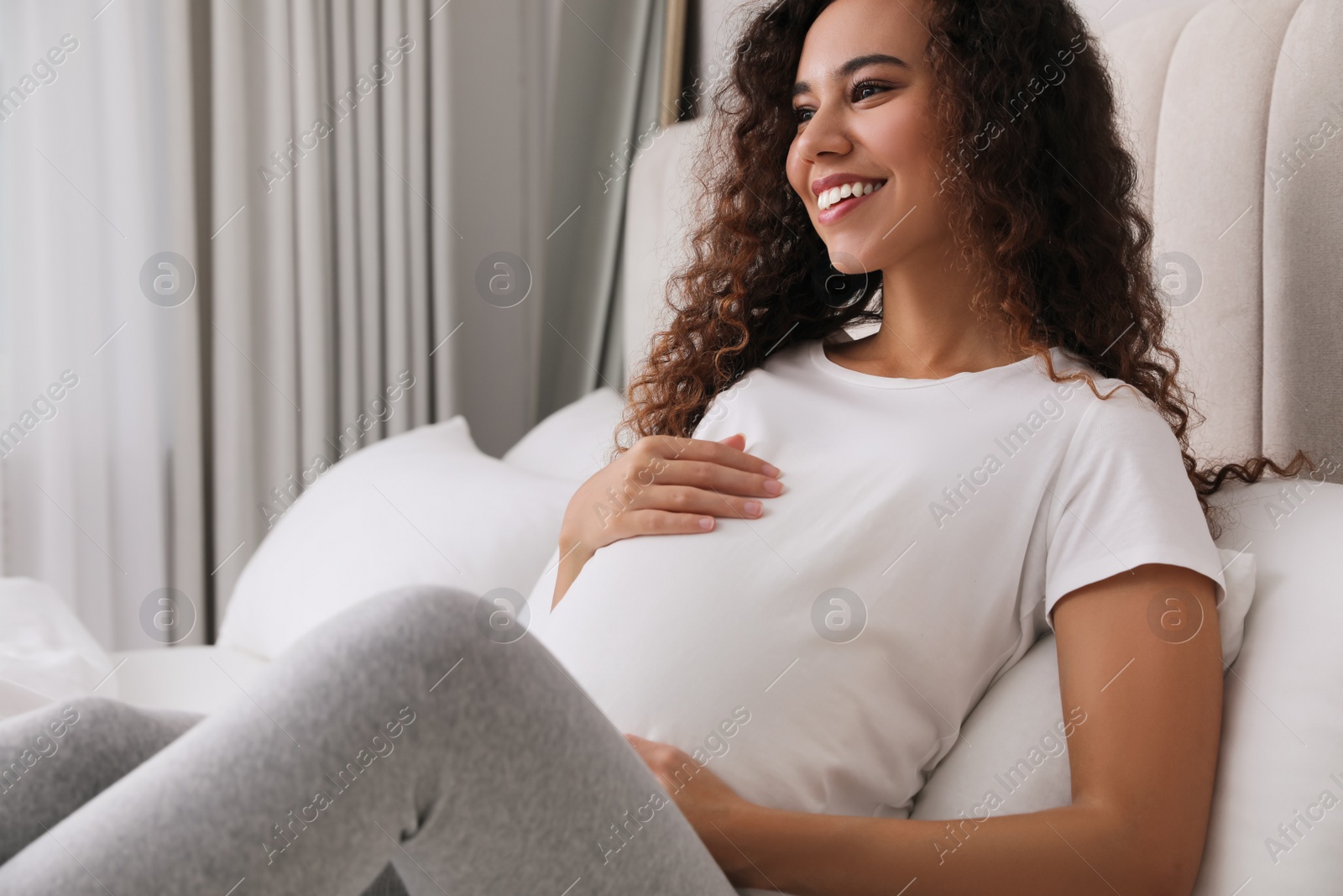 Photo of Pregnant young African-American woman sitting on bed at home