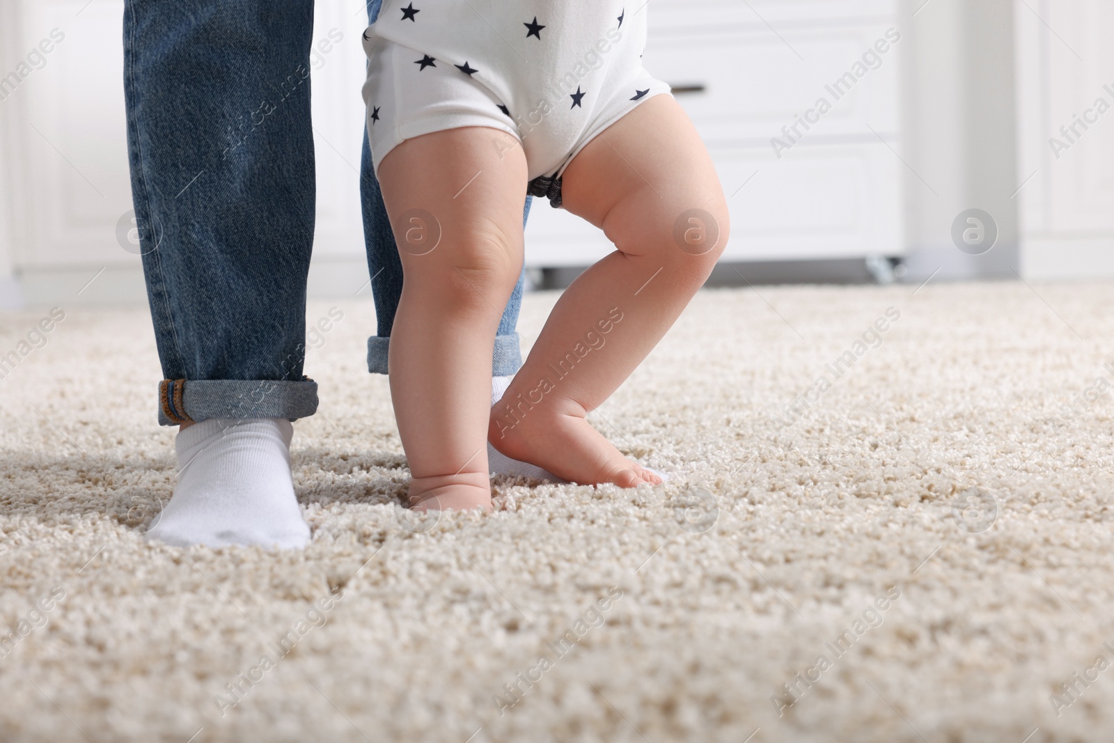 Photo of Mother supporting her baby son while he learning to walk on carpet at home, closeup. Space for text