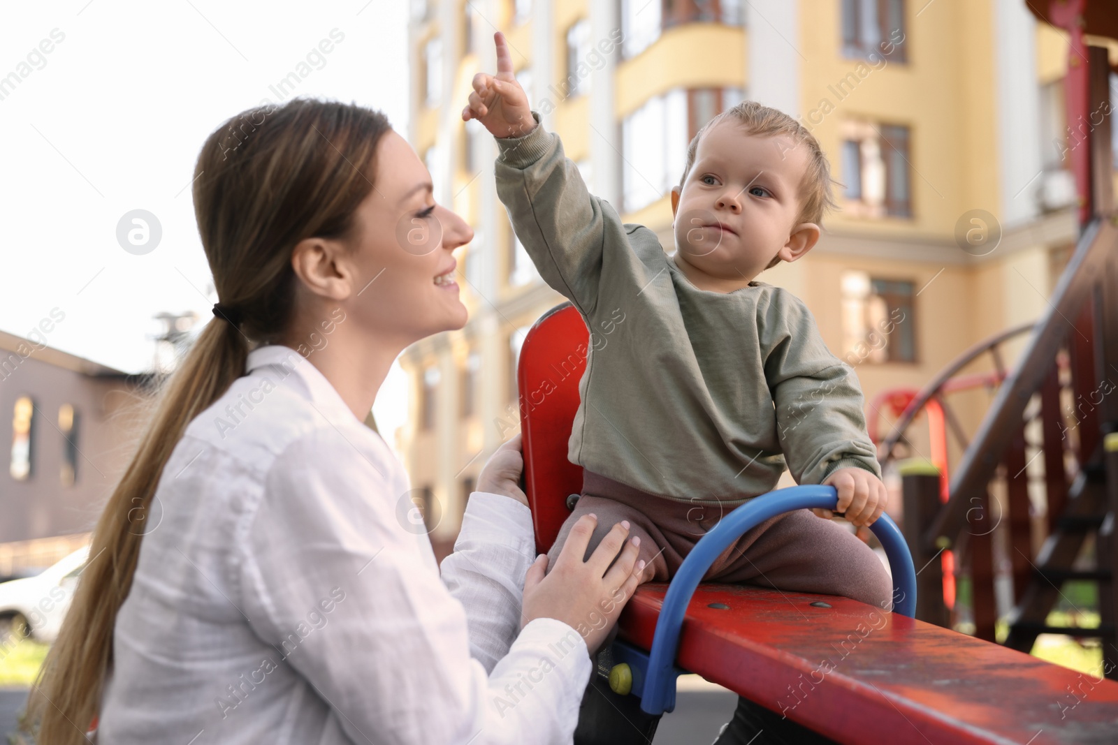 Photo of Happy nanny and cute little boy on seesaw outdoors