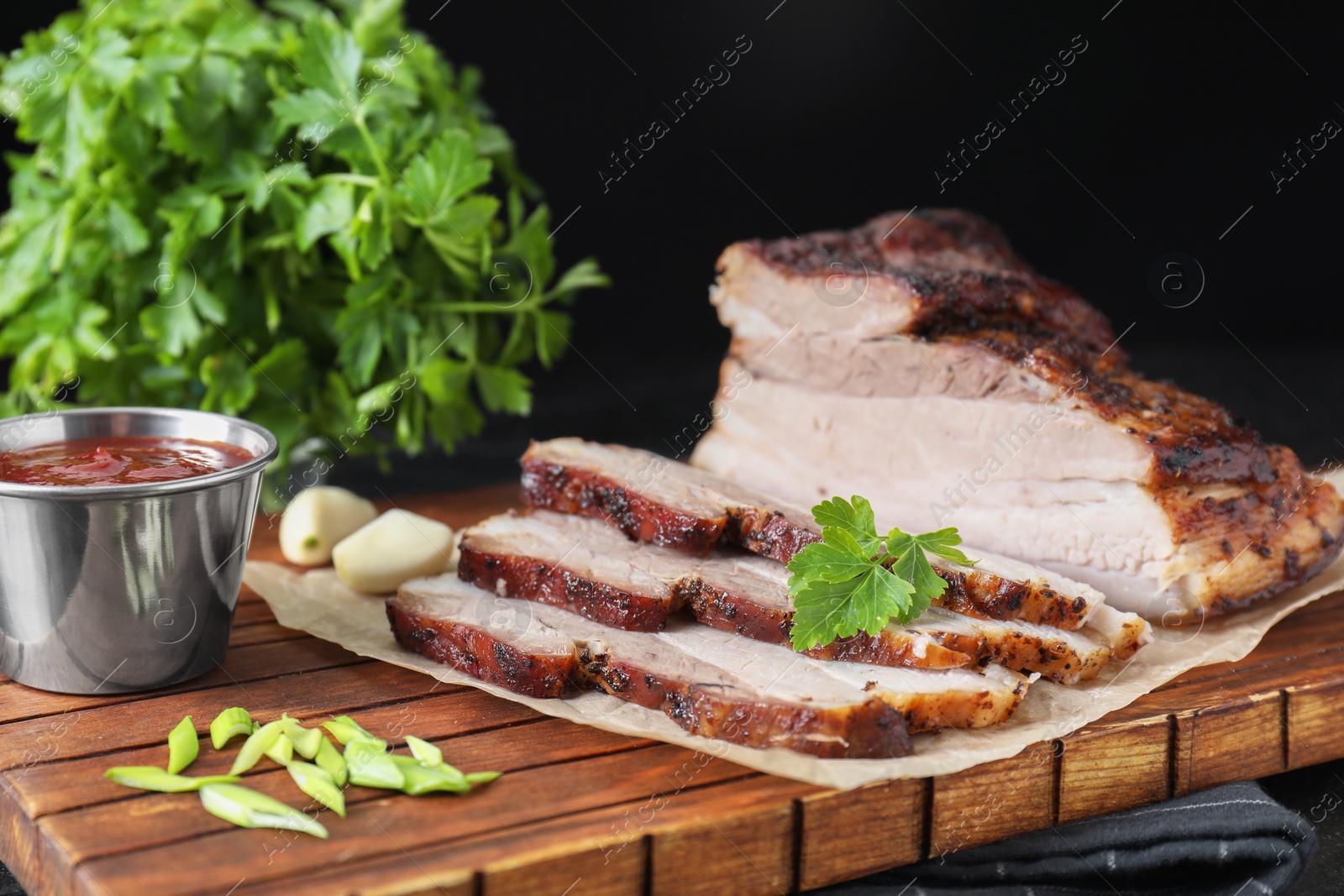 Photo of Pieces of baked pork belly served with sauce and parsley on table, closeup