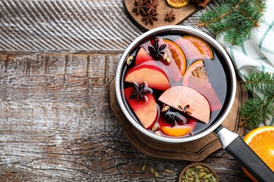 Photo of Delicious mulled wine and ingredients on wooden table, flat lay. Space for text