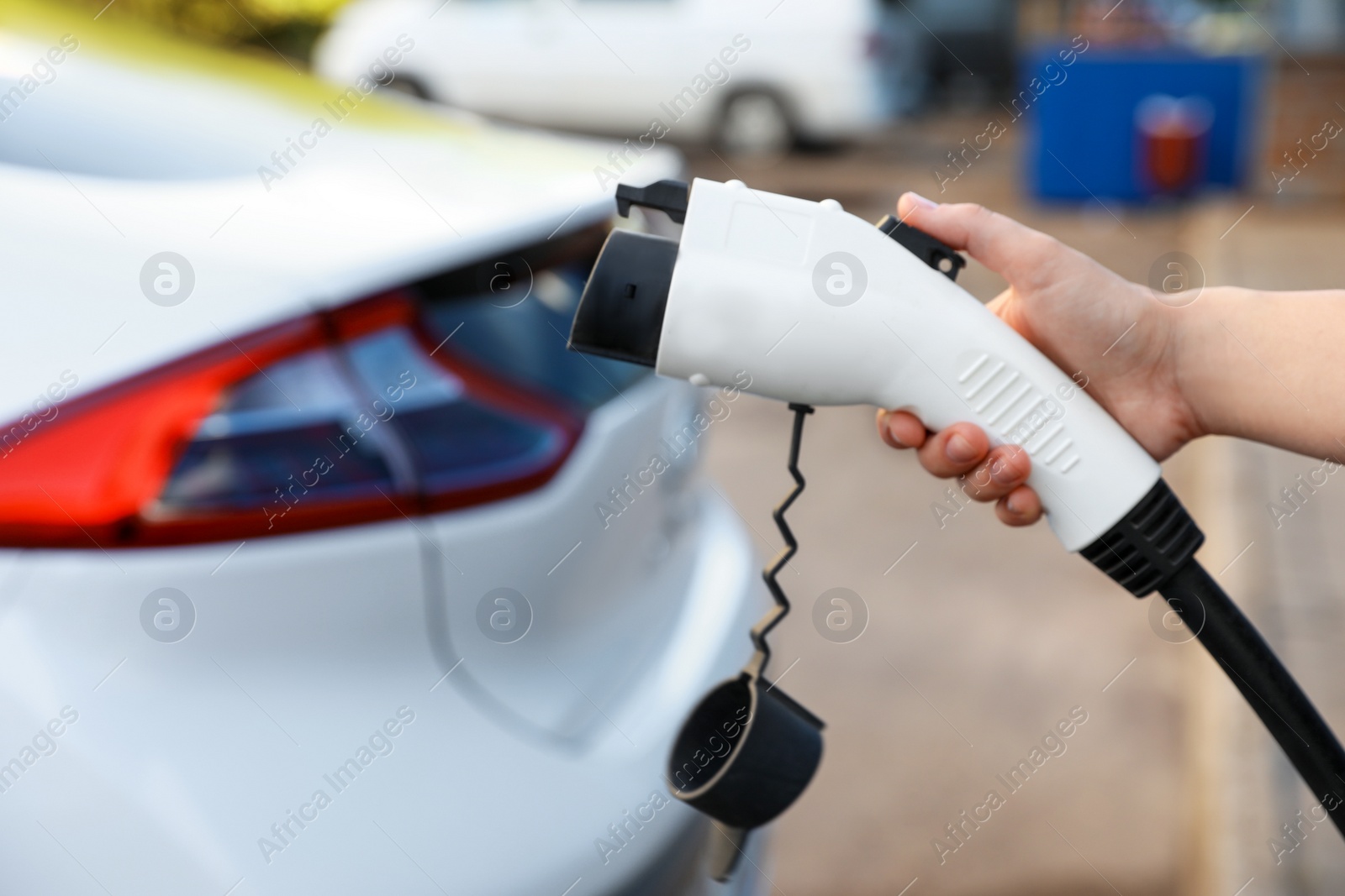 Photo of Woman holding power supply cable at electric vehicle charging station, closeup