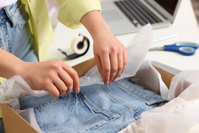 Photo of Seller packing jeans into cardboard box at workplace, closeup