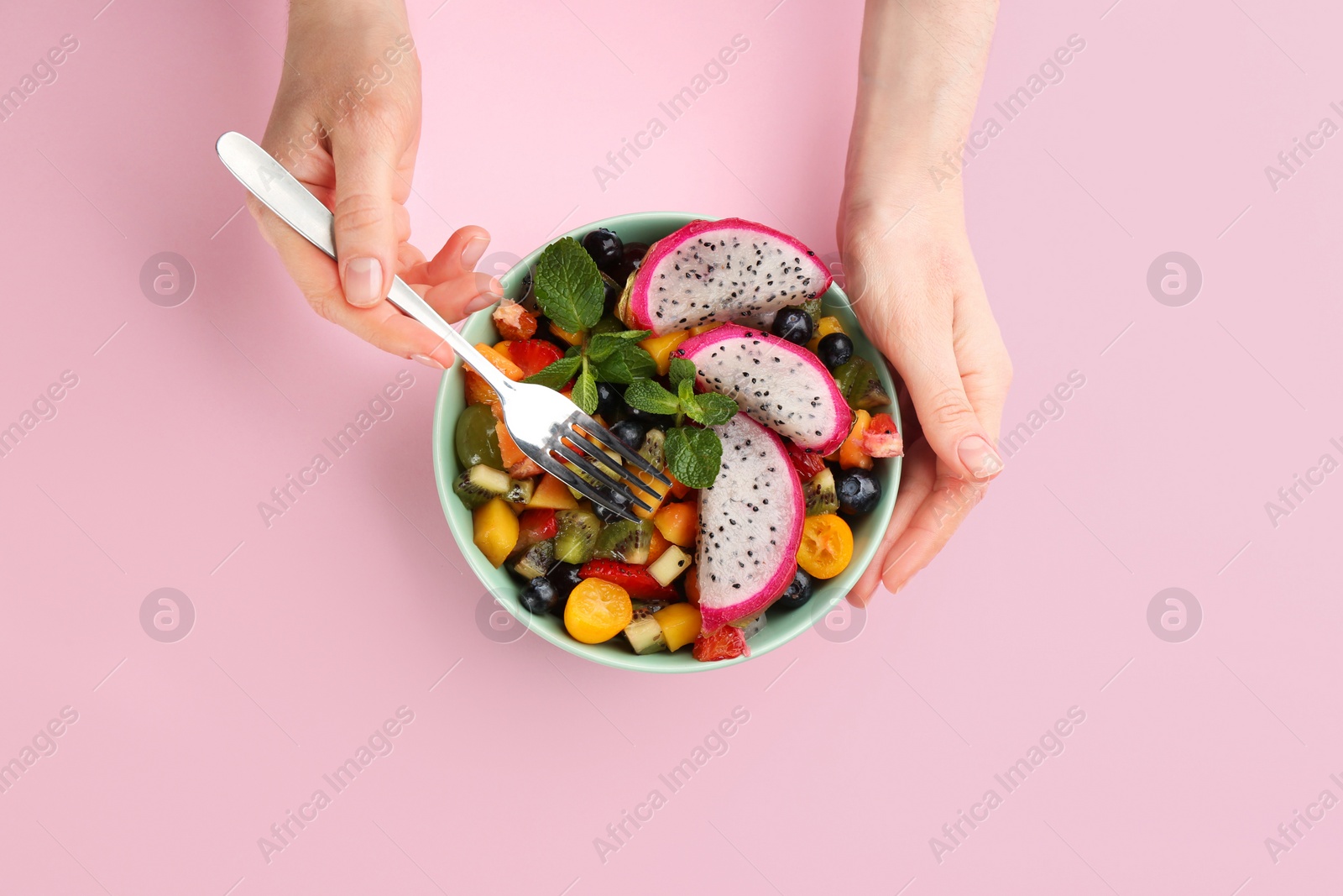 Photo of Woman with delicious exotic fruit salad on pink background, top view