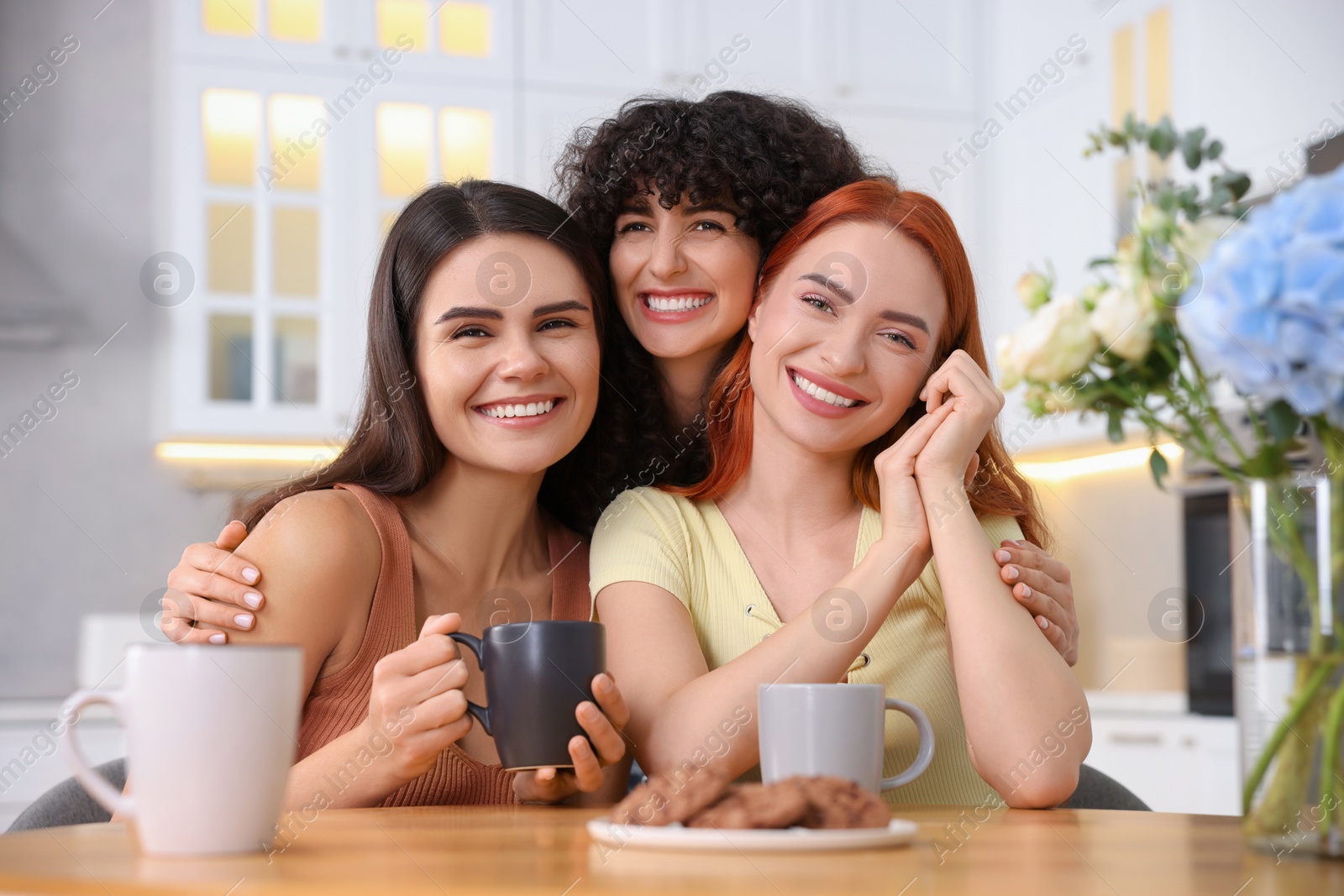 Photo of Happy young friends spending time together at table in kitchen