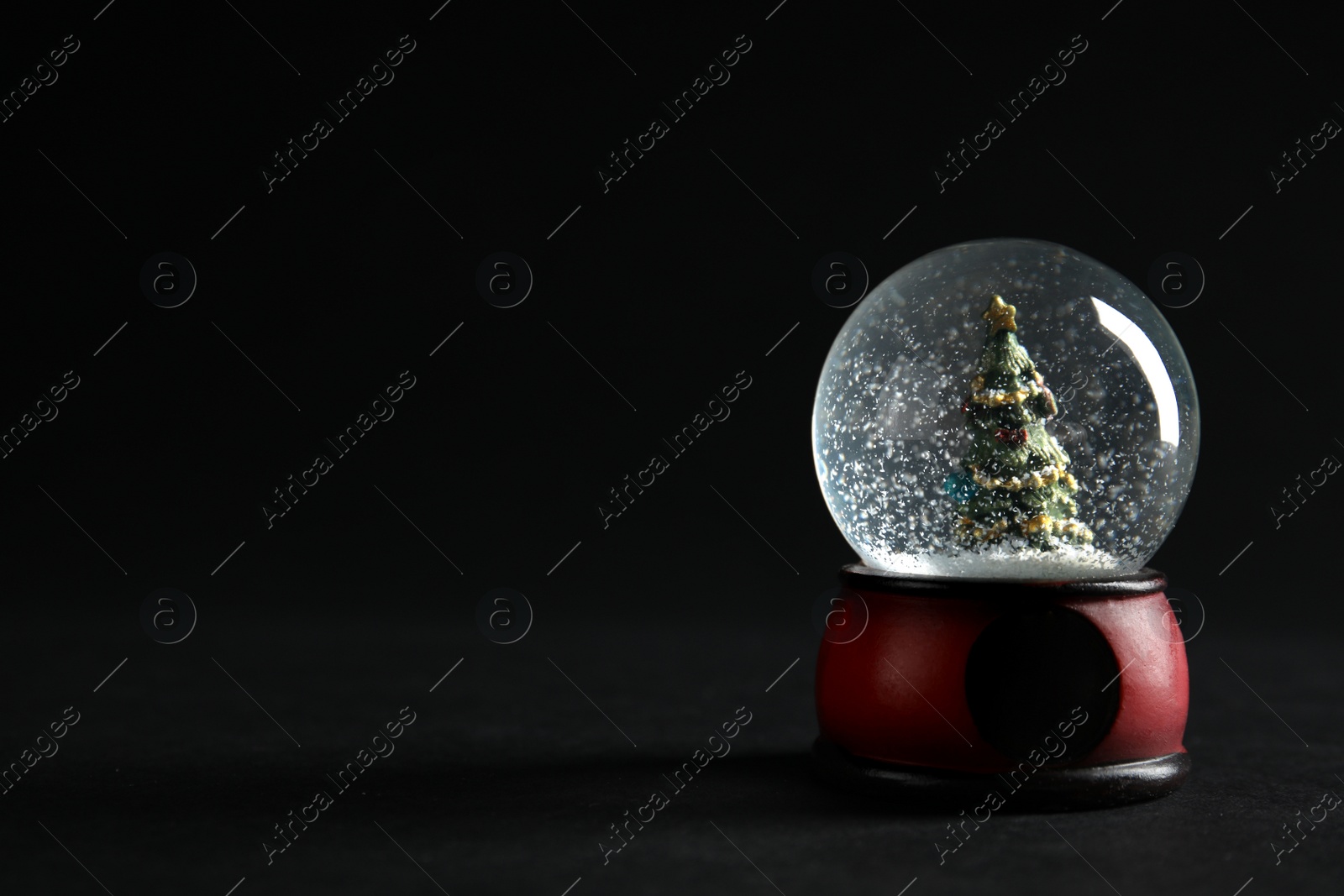 Photo of Snow globe with Christmas tree on dark background. Space for text