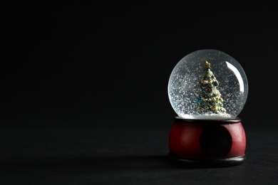 Photo of Snow globe with Christmas tree on dark background. Space for text