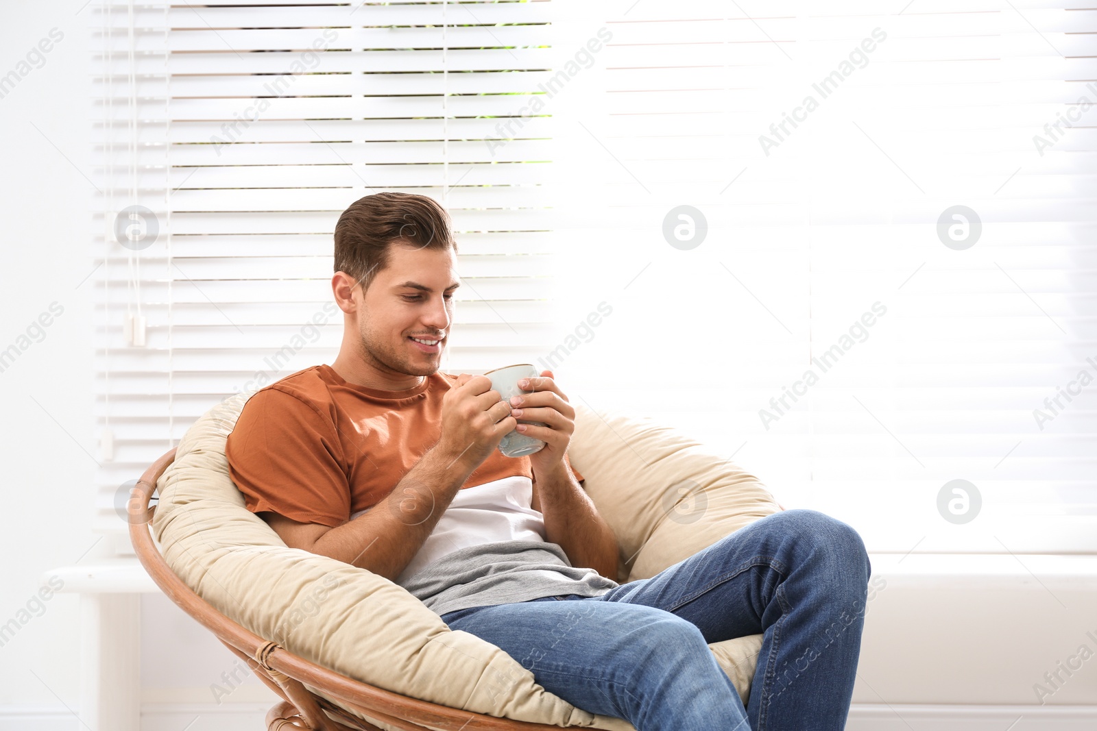 Photo of Attractive man relaxing in papasan chair near window at home