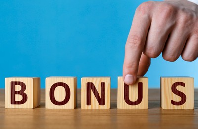 Image of Man making word Bonus of cubes with letters on wooden table, closeup