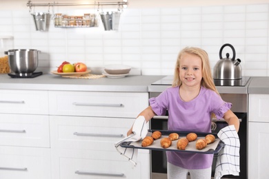 Little girl holding baking sheet with homemade oven baked croissants in kitchen