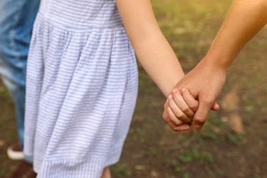 Photo of Little girl and her parents holding hands outdoors, closeup. Family weekend