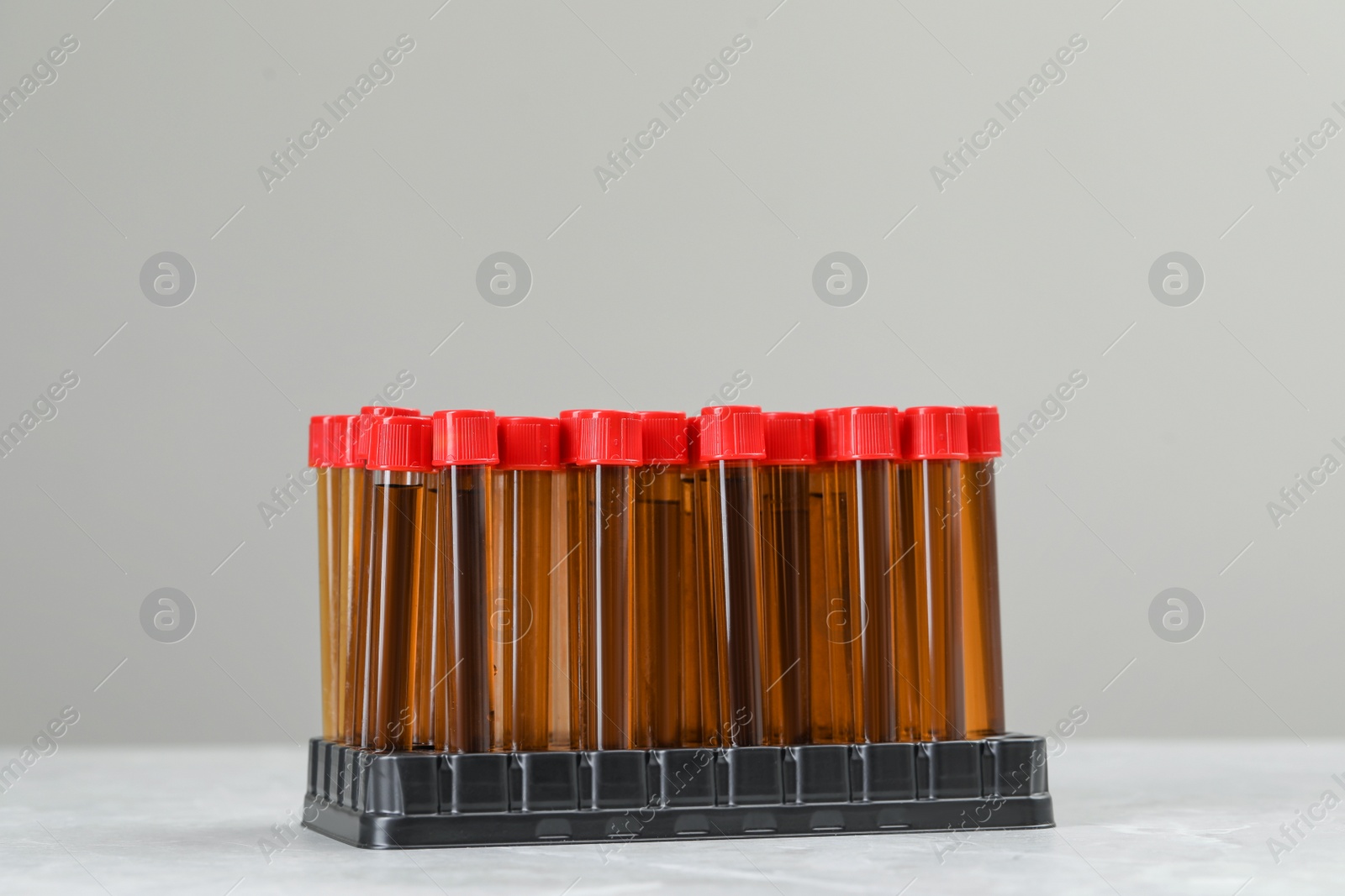 Photo of Test tubes with brown liquid in stand on white table against light background