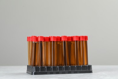 Photo of Test tubes with brown liquid in stand on white table against light background