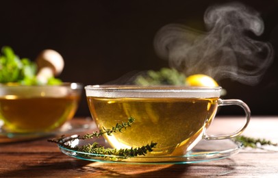 Photo of Cup of aromatic herbal tea and fresh thyme on wooden table