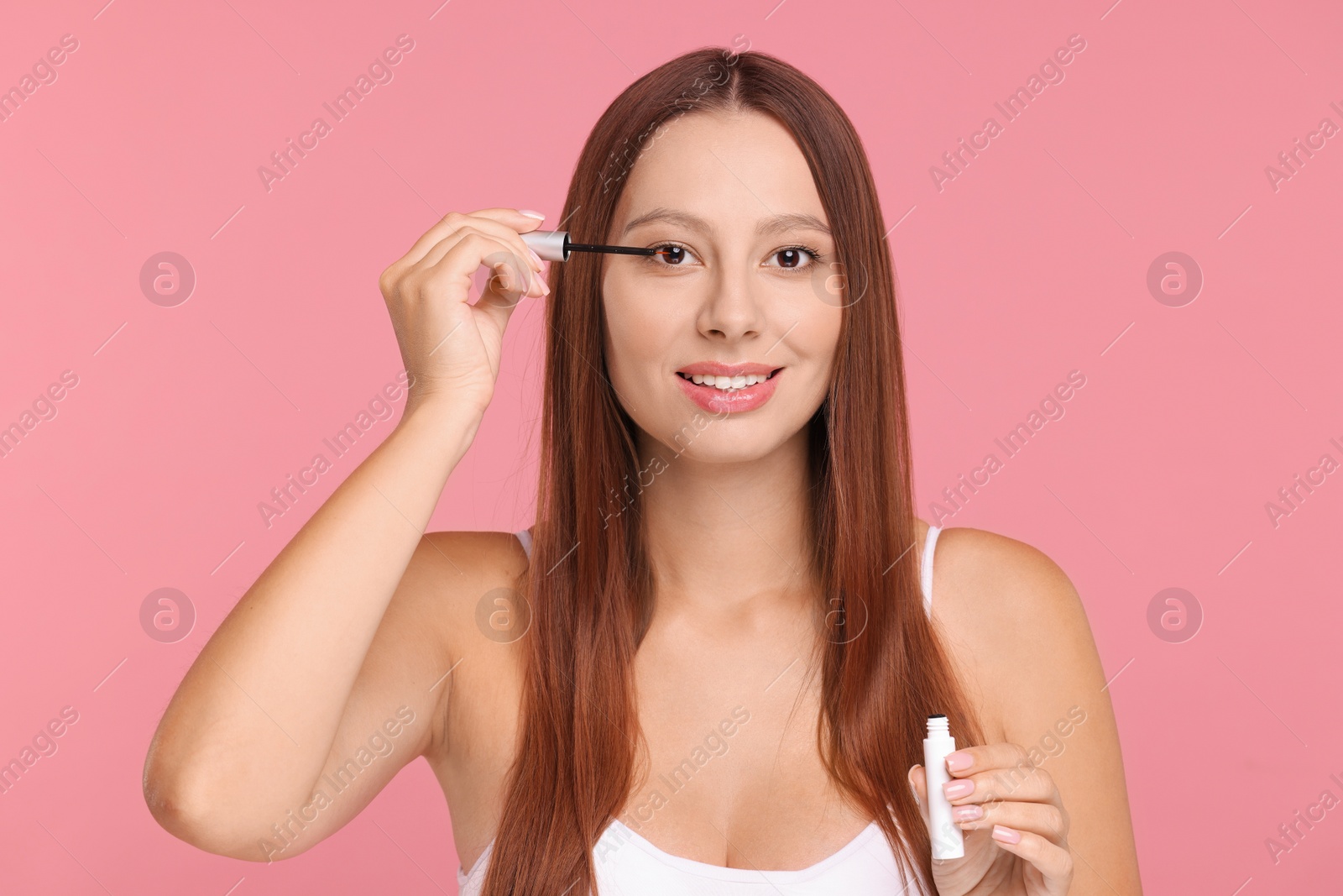 Photo of Beautiful woman applying serum onto eyelashes on pink background