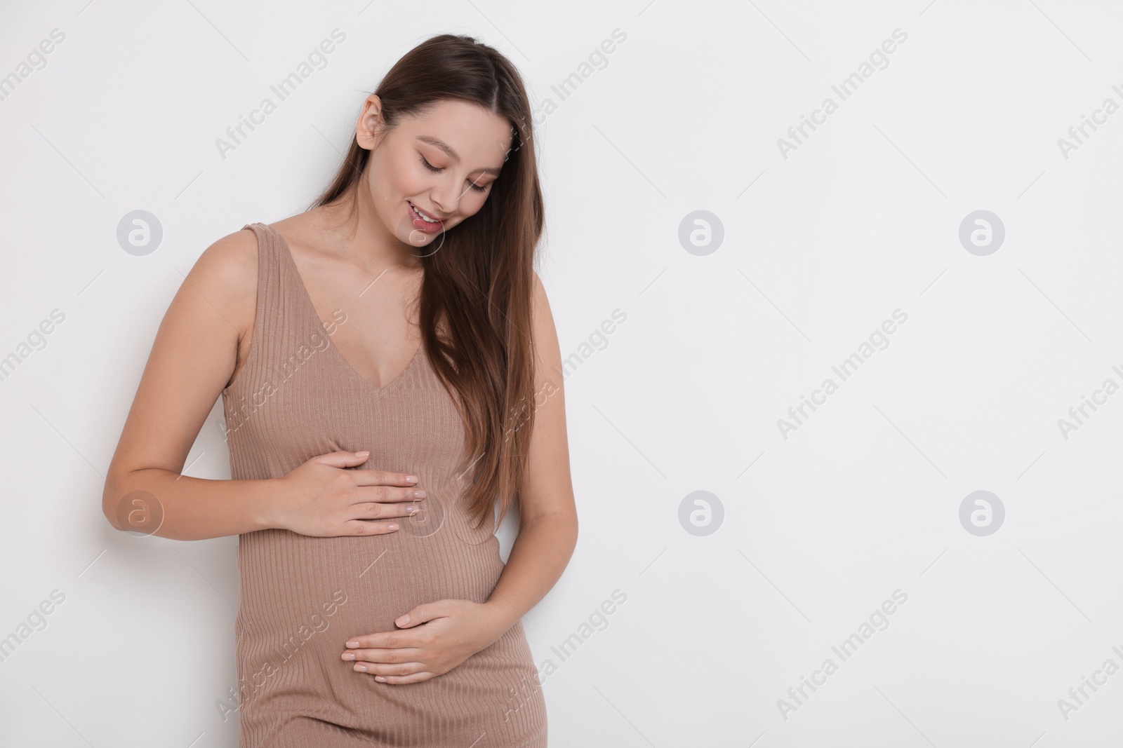 Photo of Beautiful pregnant woman in beige dress on white background, space for text
