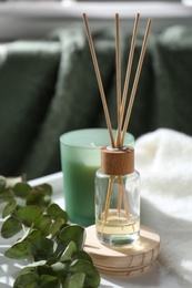 Photo of Reed air freshener, candle and eucalyptus branches on tray indoors