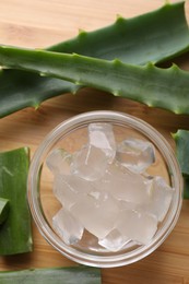 Aloe vera gel and slices of plant on wooden table, flat lay