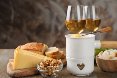 Pot of tasty cheese fondue and products on wooden table