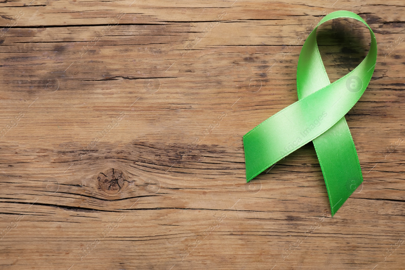 Photo of World Mental Health Day. Green ribbon on wooden background, top view with space for text