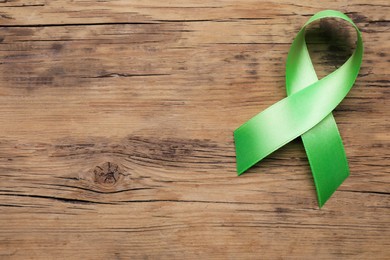 World Mental Health Day. Green ribbon on wooden background, top view with space for text