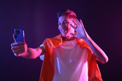 Photo of Young man taking selfie on dark background in neon lights