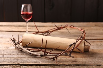 Crown of thorns, old scroll and glass with wine on wooden table, selective focus