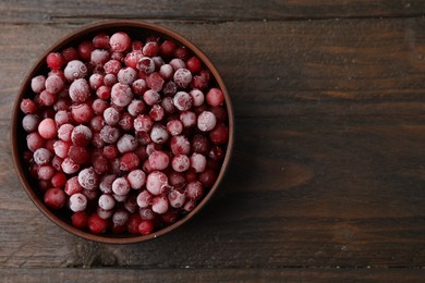 Photo of Frozen red cranberries in bowl on wooden table, top view. Space for text