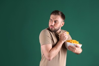 Photo of Greedy young man hiding bowl with chips on green background