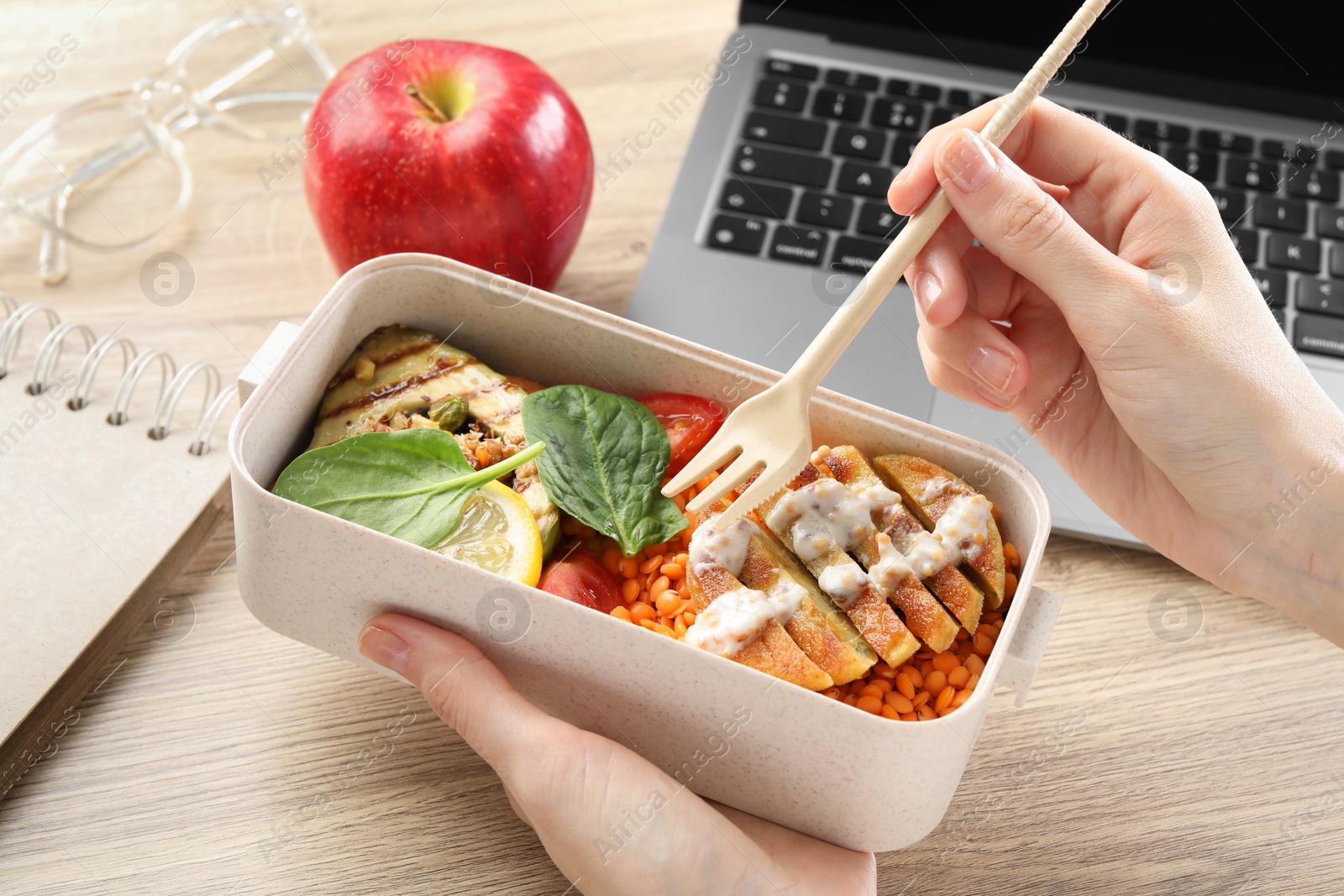 Photo of Woman eating healthy products high in vegetable fats near laptop at wooden table, closeup