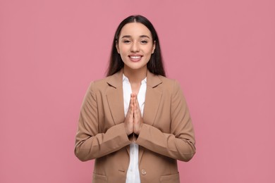 Thank you gesture. Beautiful grateful woman with hands clasped together on pink background