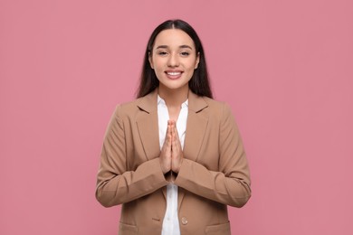 Photo of Thank you gesture. Beautiful grateful woman with hands clasped together on pink background