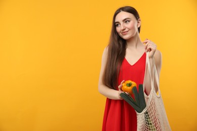 Woman with string bag of fresh vegetables on orange background, space for text