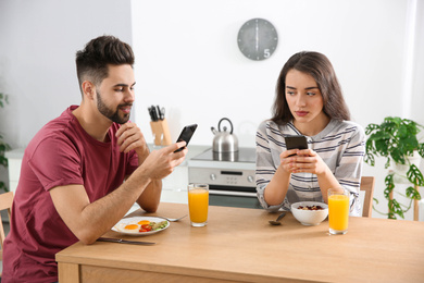 Photo of Young couple with smartphones having breakfast at home