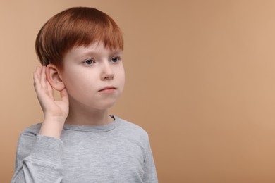 Photo of Little boy with hearing problem on pale brown background, space for text