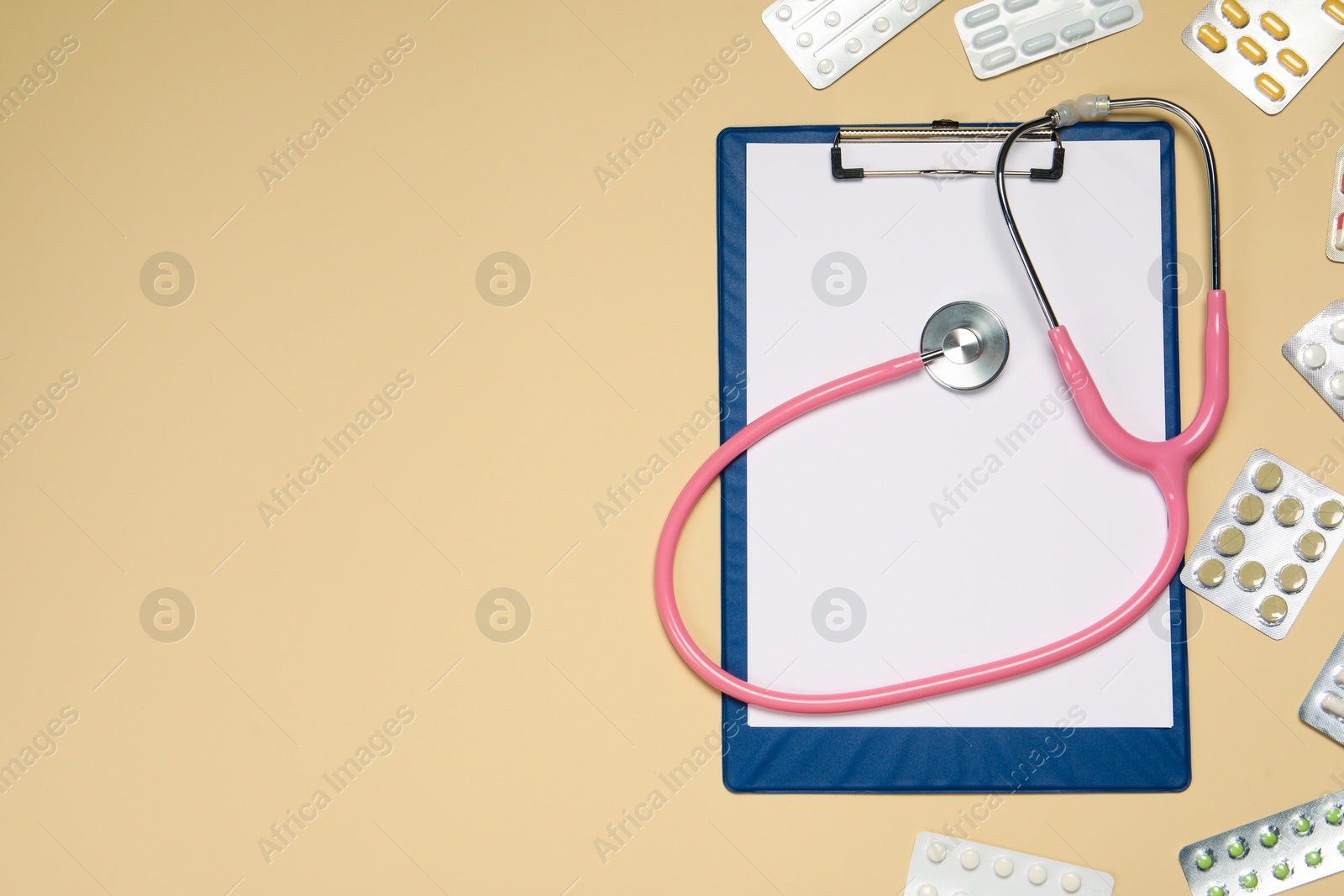 Photo of Stethoscope, clipboard and pills on beige background, flat lay. Space for text