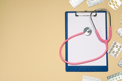 Stethoscope, clipboard and pills on beige background, flat lay. Space for text