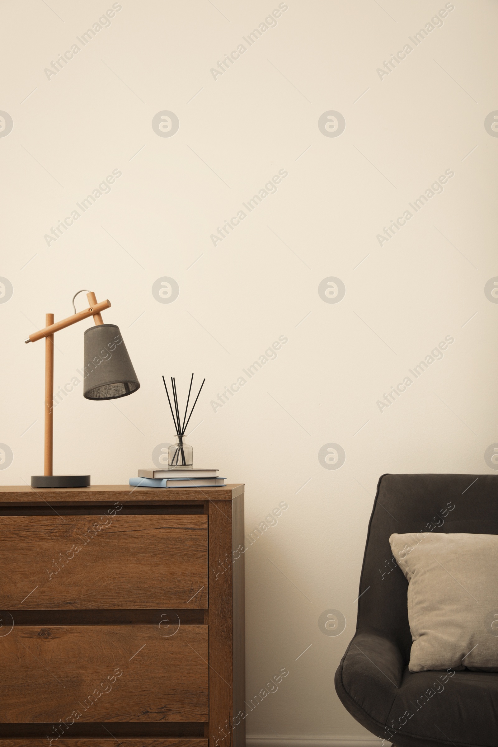 Photo of Modern chest of drawers and armchair near white wall in room