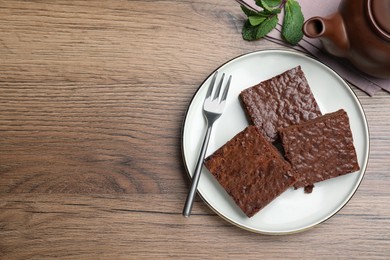 Photo of Delicious chocolate brownies served on wooden table, flat lay. Space for text