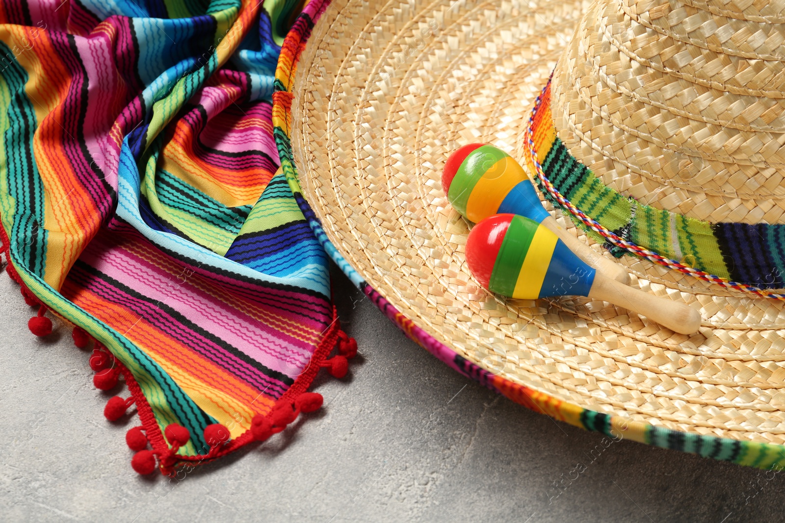 Photo of Mexican sombrero hat, maracas and colorful poncho on grey textured background