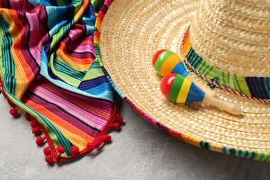 Photo of Mexican sombrero hat, maracas and colorful poncho on grey textured background