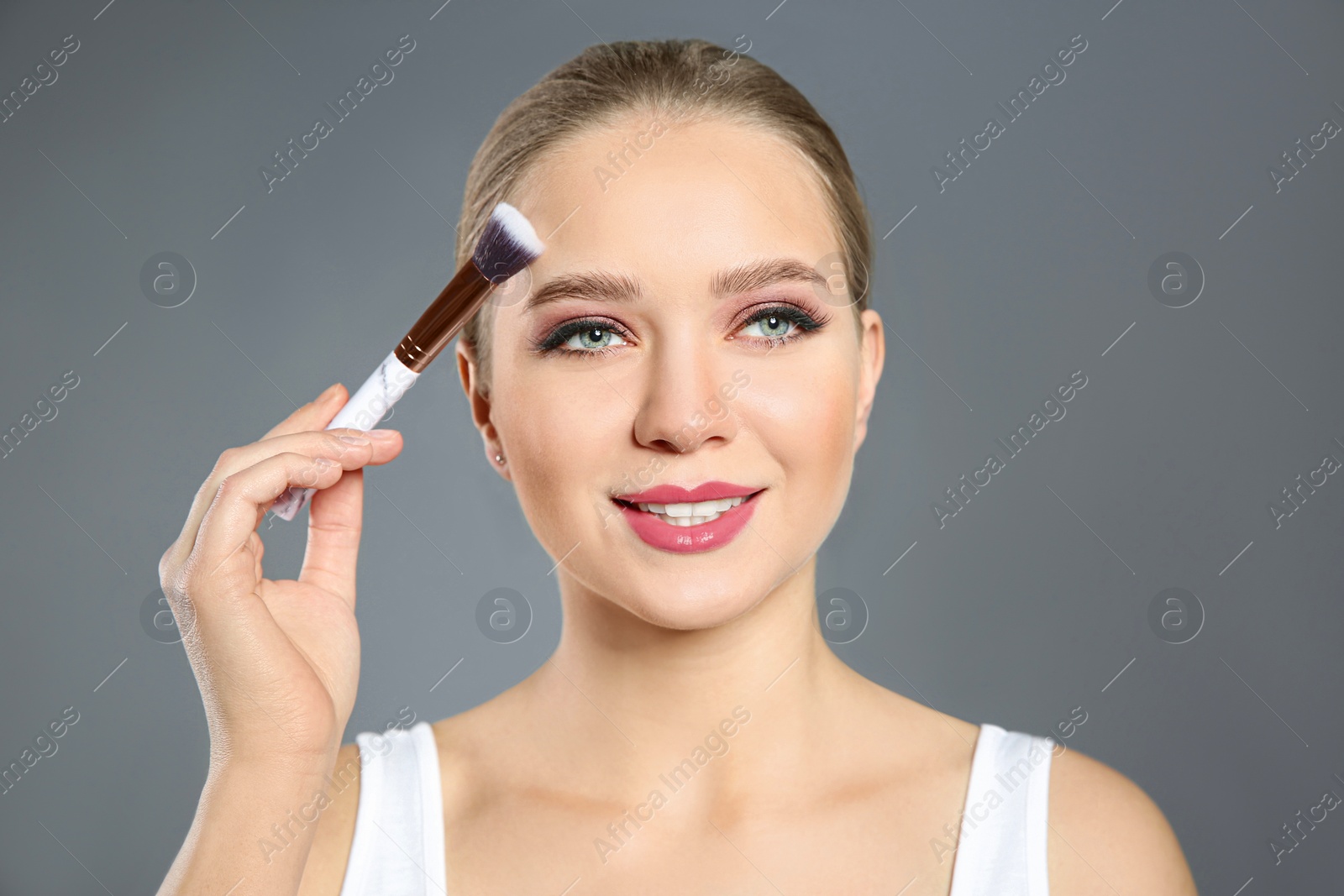 Photo of Beautiful woman applying makeup with brush on light grey background