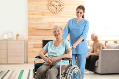 Nurse assisting elderly woman in wheelchair at retirement home. Space for text